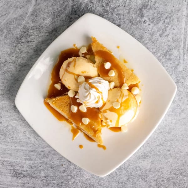 Warm cookie pie slices with vanilla ice cream, whipped cream, caramel, and white chocolate chips.