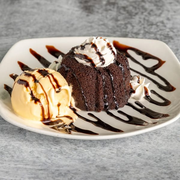 Chocolate lava cake topped with whipped cream and chocolate syrup, served with vanilla ice cream.