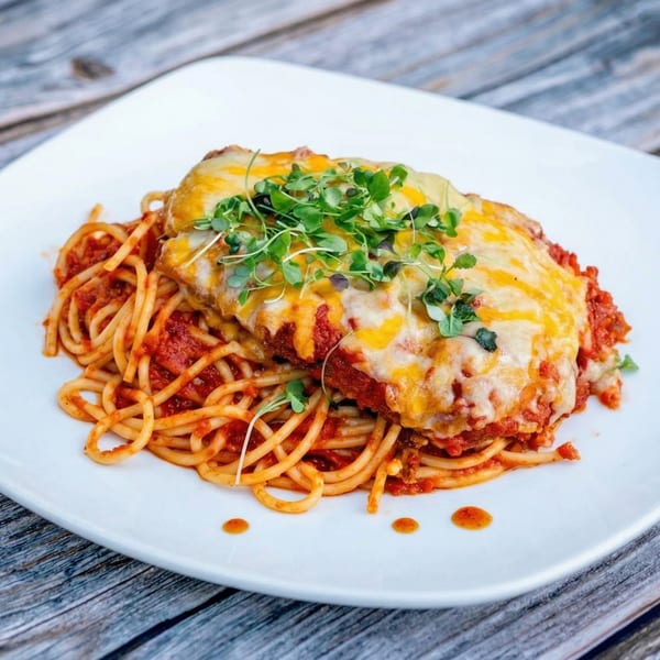 Chicken parmesan with spaghetti and tomato sauce, topped with melted cheese and microgreens on a white plate.