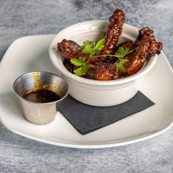 Glazed chicken wings with parsley in a white bowl, with a side of dipping sauce.
