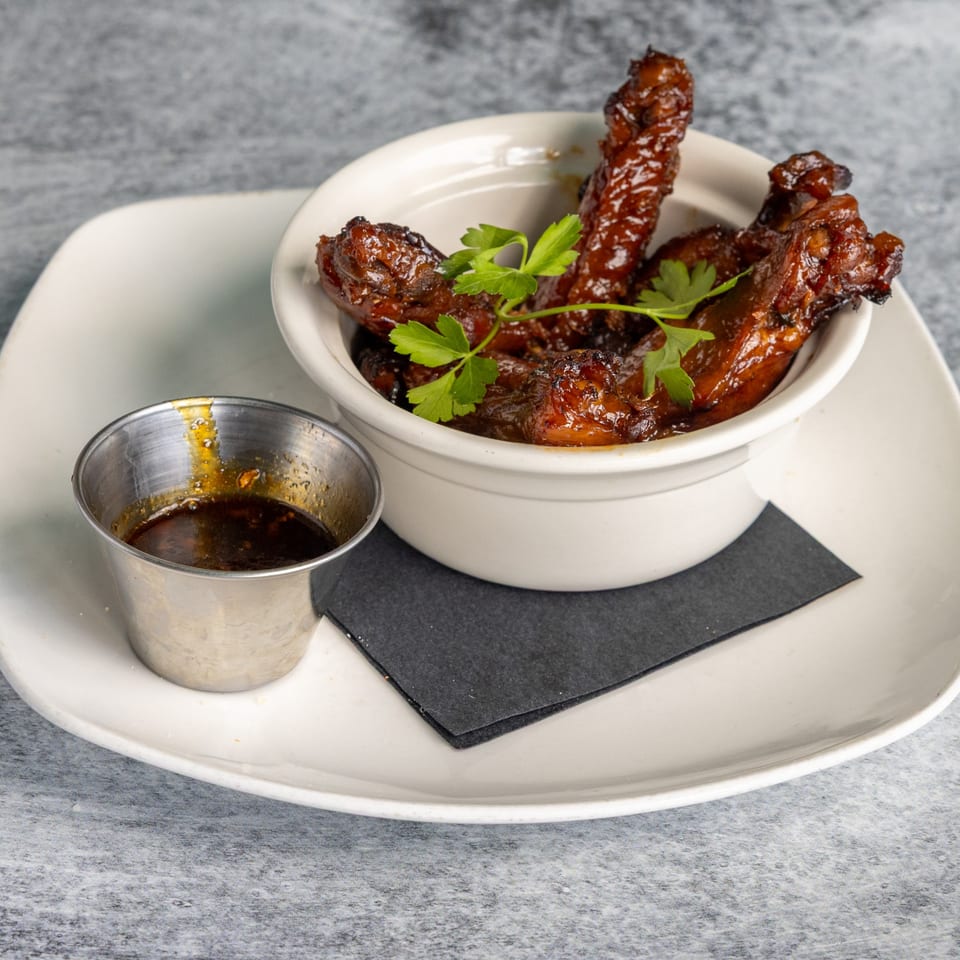 Glazed chicken wings with parsley in a white bowl, with a side of dipping sauce.