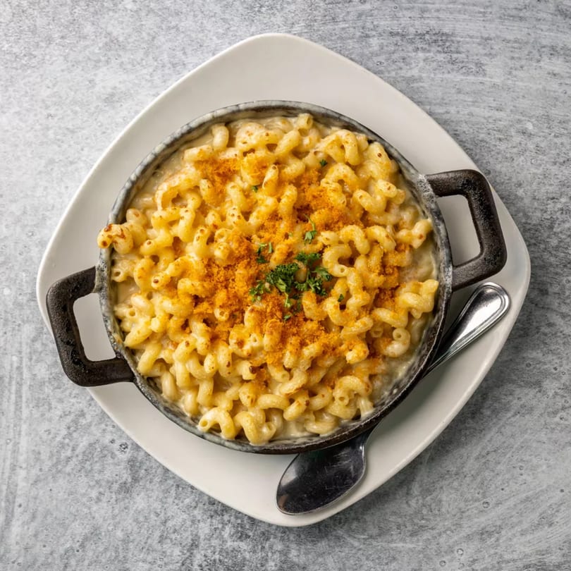 Creamy macaroni and cheese in a black cast iron dish, topped with breadcrumbs and parsley.