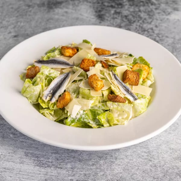 Caesar salad with romaine lettuce, croutons, parmesan cheese, and anchovies in a white bowl.