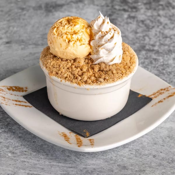 A dessert in a white bowl with crumble, a scoop of ice cream, and whipped cream.