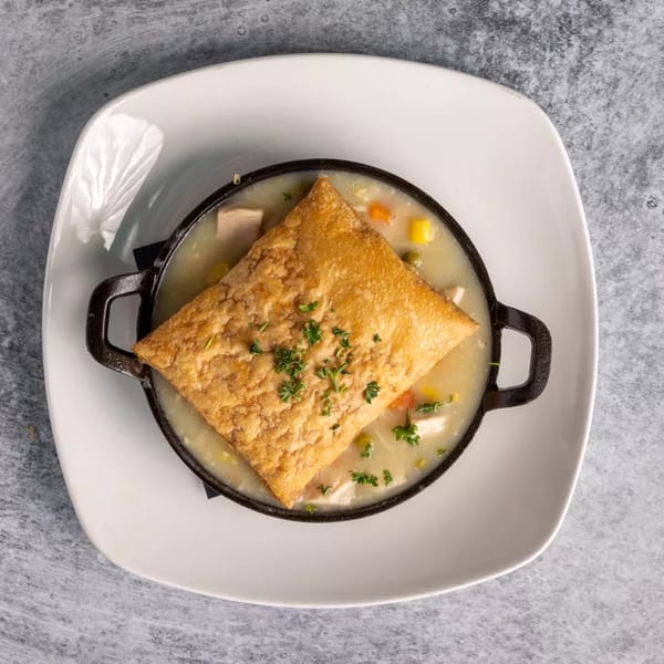Creamy chicken pot pie with a golden-brown puff pastry crust, served in a black cast iron dish.