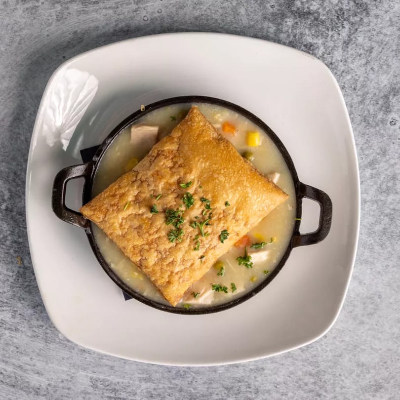 Creamy chicken pot pie with a golden-brown puff pastry crust, served in a black cast iron dish.