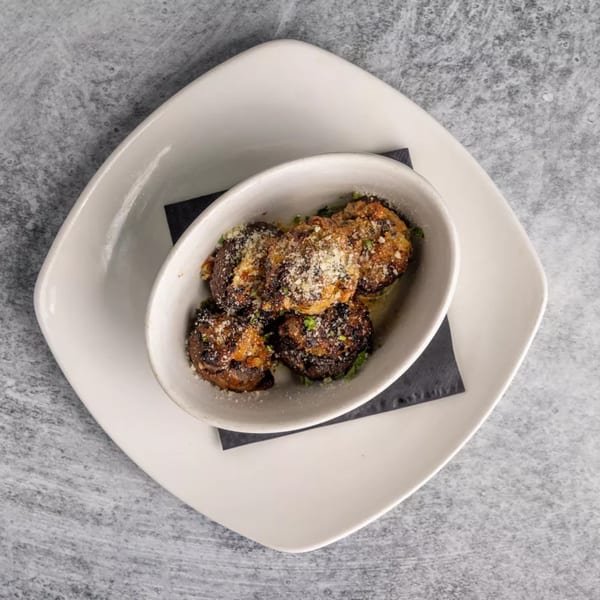 Top-down view of a white bowl filled with five stuffed mushrooms, sprinkled with cheese and herbs.