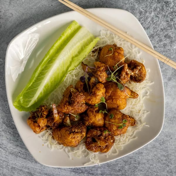 Crispy fried cauliflower florets with microgreens and lettuce on a white plate with chopsticks.