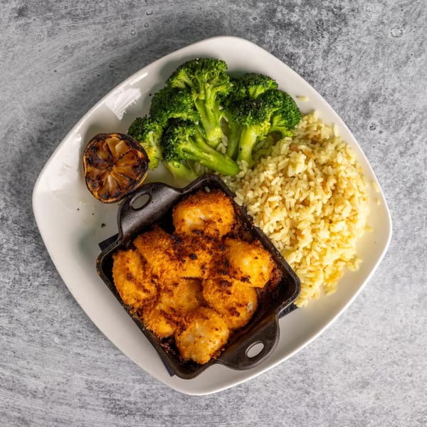 Baked scallops in a cast iron dish with rice, broccoli, and a charred lemon wedge.