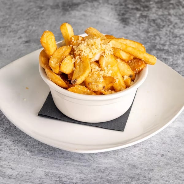 A white bowl of golden french fries, sprinkled with parmesan cheese, on a white plate.