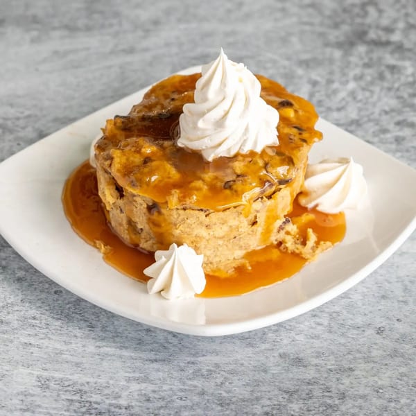 Bread pudding with caramel sauce and whipped cream on a white plate.