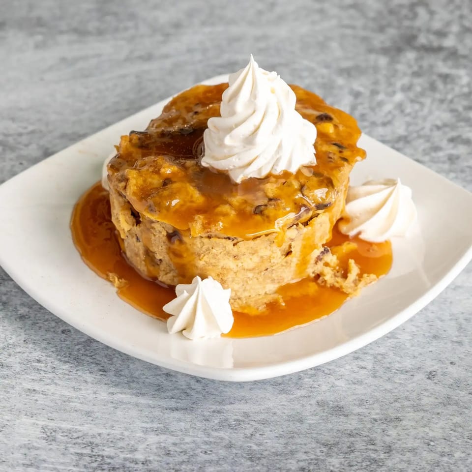 Bread pudding with caramel sauce and whipped cream on a white plate.