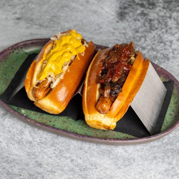 Two hot dogs on a green plate, one with mustard and sauerkraut, the other with caramelized onions.