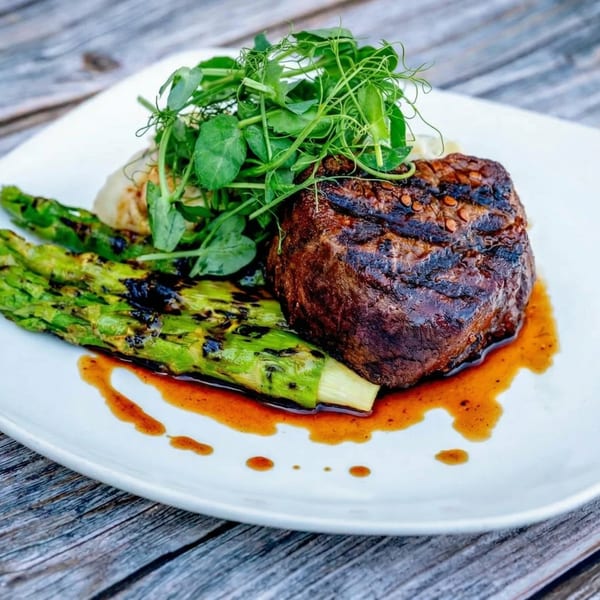 Grilled steak with asparagus, mashed potatoes, and pea shoots on a white plate.