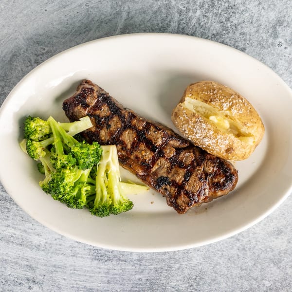 Grilled steak with broccoli and a baked potato with butter and salt on a white plate.