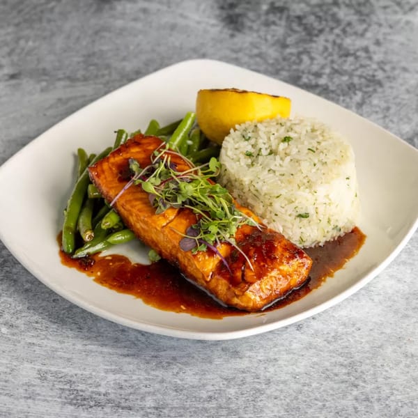 Glazed salmon with green beans, white rice, and a lemon wedge on a white plate.