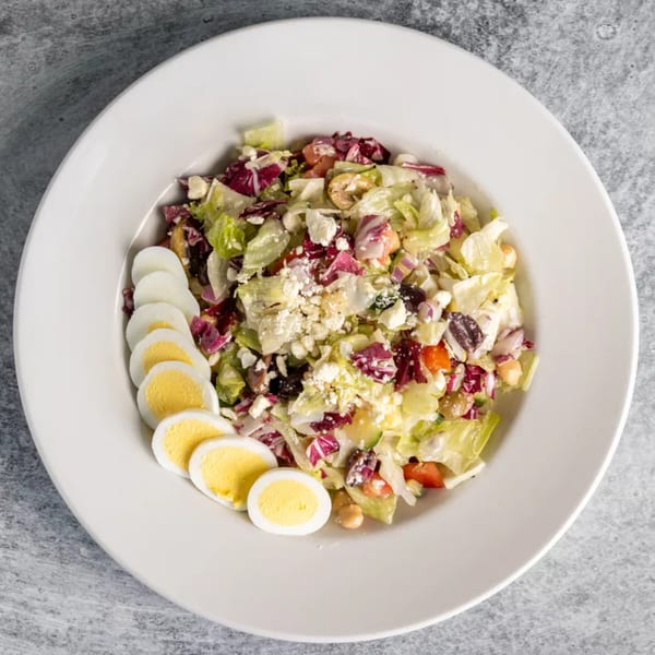 Overhead view of a salad with mixed greens, feta, and sliced hard-boiled eggs on a white plate.
