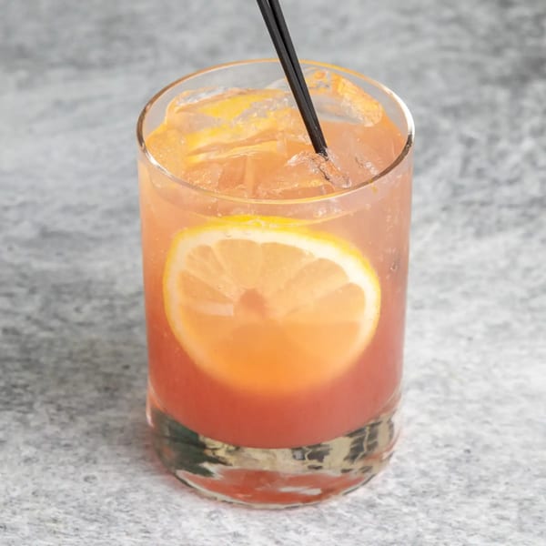 A vibrant orange cocktail with ice, a lemon slice, and a black straw in a clear glass.